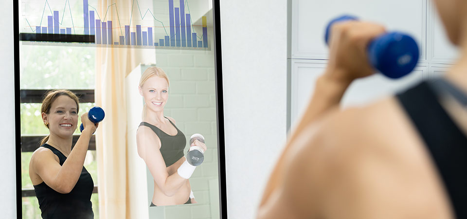 A woman exercising in a connected mirror displaying a live stream of a virtual coach and health analytics. 