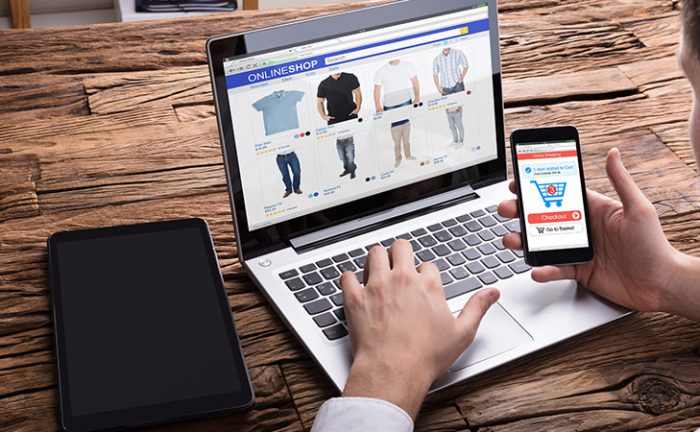 An image of a man browsing products on his laptop while purchasing items on his smartphone.