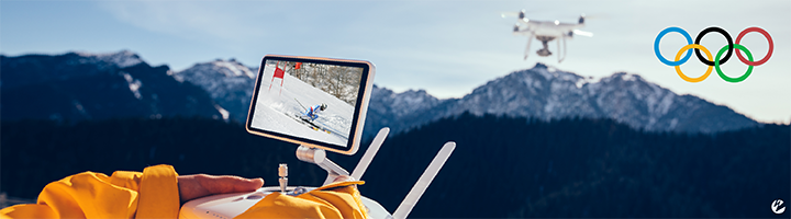 A person in a ski coat operating a drone over snow-covered mountains with an Olympic logo in the top-right corner.